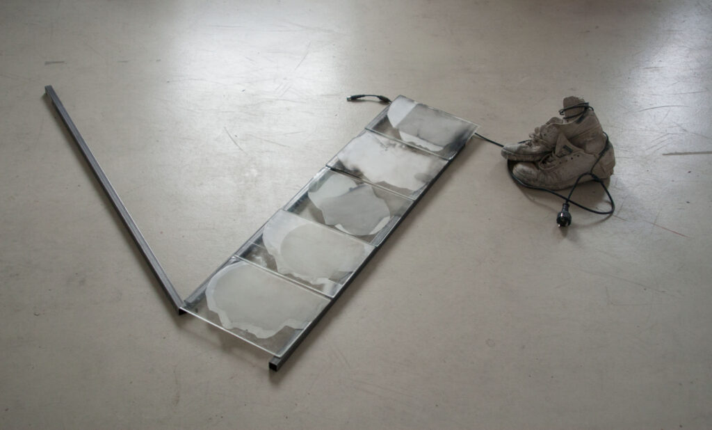 Allein zu Hause, 2024, 140x120x20cm, Vierkantrohr Stahl, Keramische Farben und Sandstrahlen auf Glas, Laptop Ladekabel, Schuhe und Ton